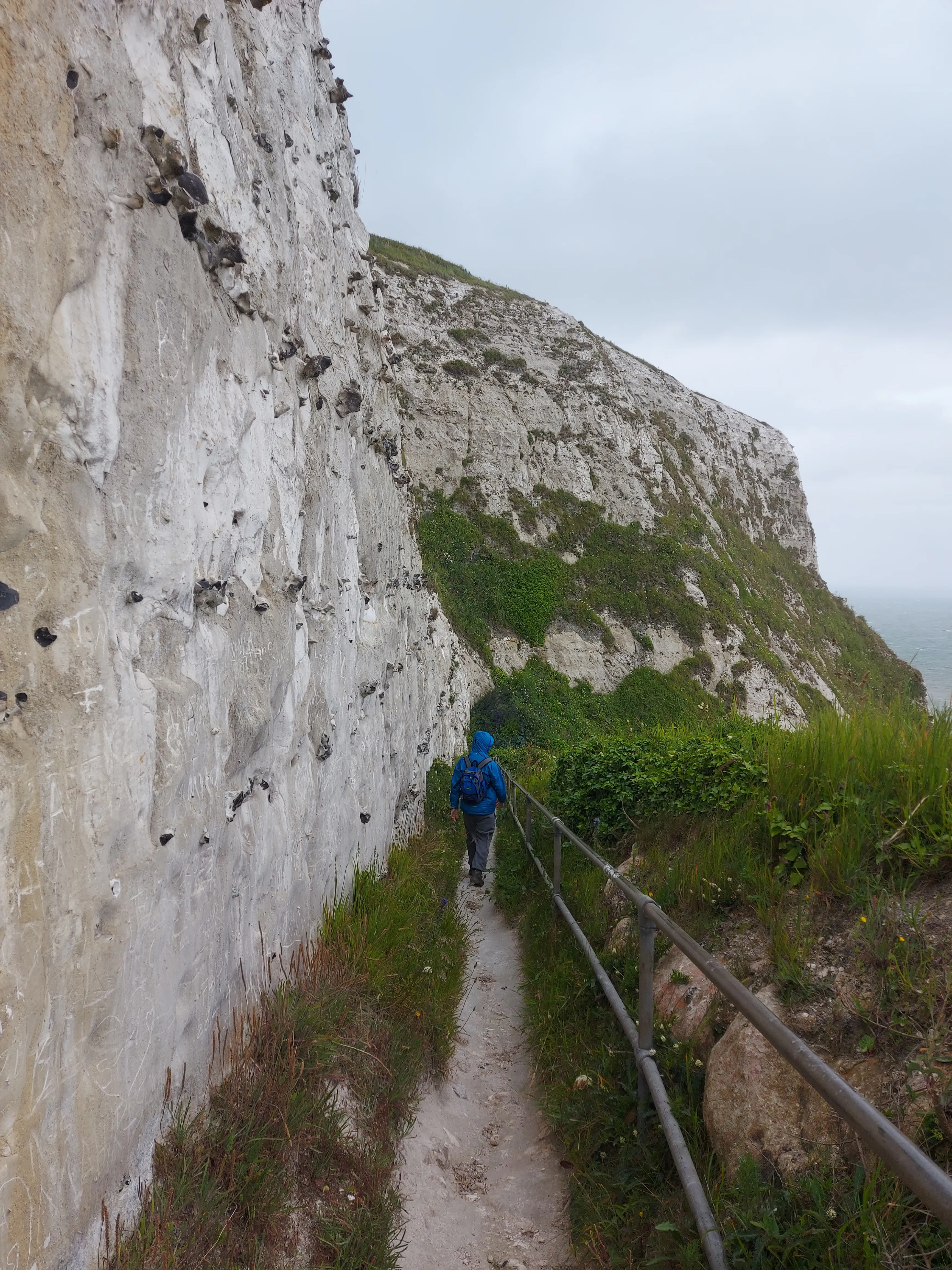 Path on the cliff face part of Langdon Stairs that descends to Langdon Bay, with a person giving their back to the camera dressed in blue raincoat.
